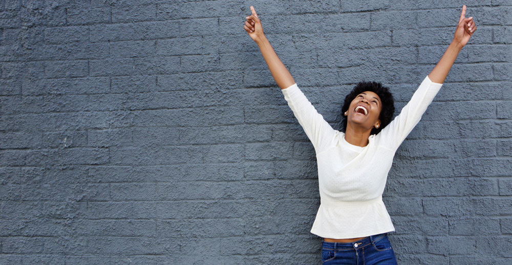 photo of a woman happy and smiling with her hands in the air as if she’s celebrating
