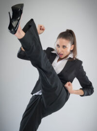 woman in business suit and high heels with a determined expression doing a high kick