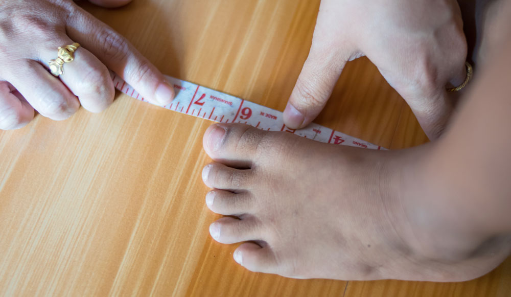 Someone holding a tape measure next to a bare foot