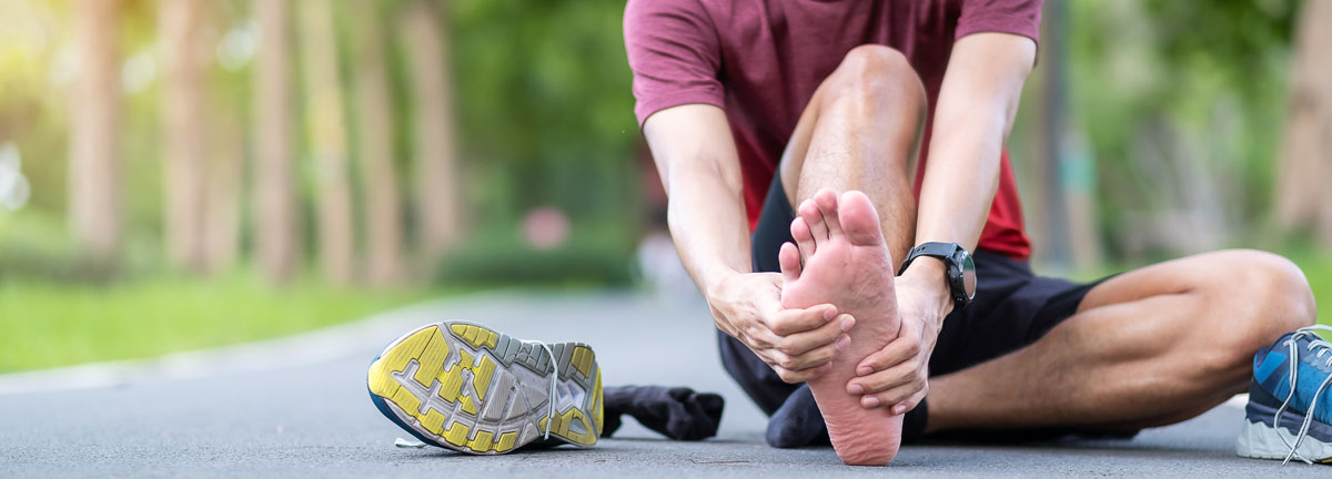 runner sitting on ground in park holding the sore arch of his foot
